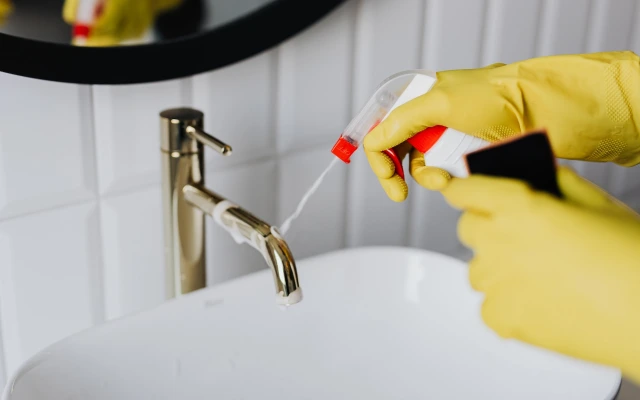 Hands with gloves spraying disinfectant cleaner on sink